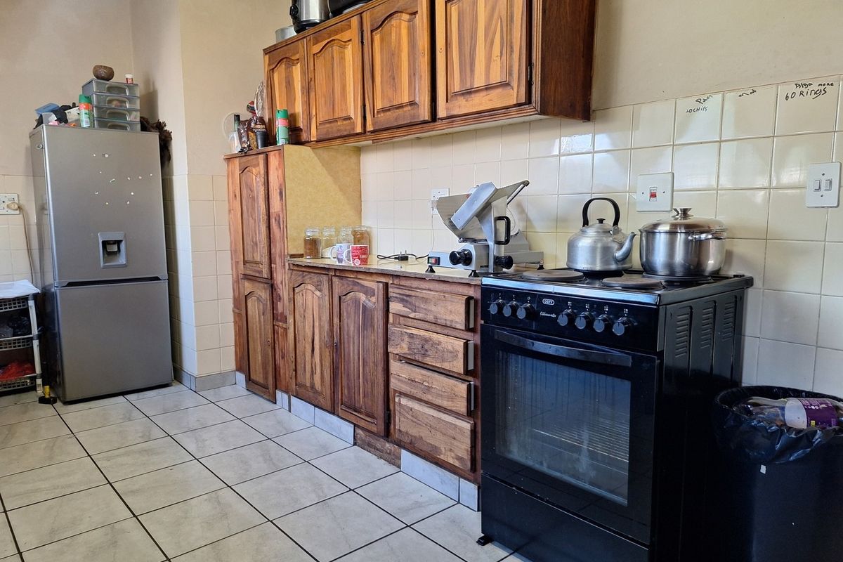 A functional kitchen featuring wooden cabinetry, tiled backsplash, and tiled flooring, equipped with a freestanding oven and hob.