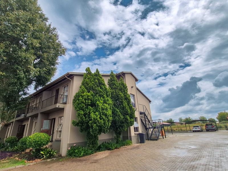 Exterior view of an apartment complex featuring paved parking, covered bays, external staircases, and established garden landscaping.