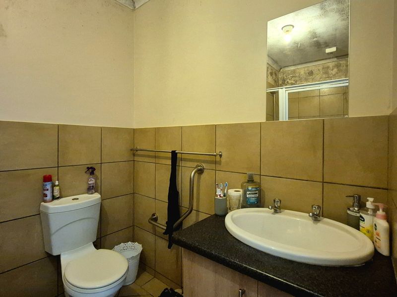 A functional bathroom featuring a vanity with basin, toilet, and tiled walls, showing signs of ceiling water damage requiring maintenance.