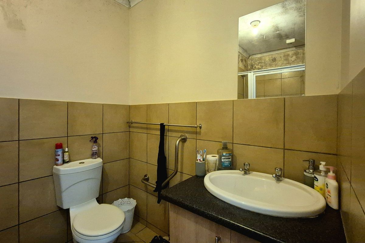 A functional bathroom featuring a vanity with basin, toilet, and tiled walls, showing signs of ceiling water damage requiring maintenance.