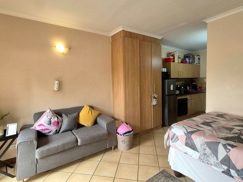 Open-plan studio apartment featuring tiled flooring, built-in wardrobe storage, and a compact kitchen area with integrated oven and cabinetry.