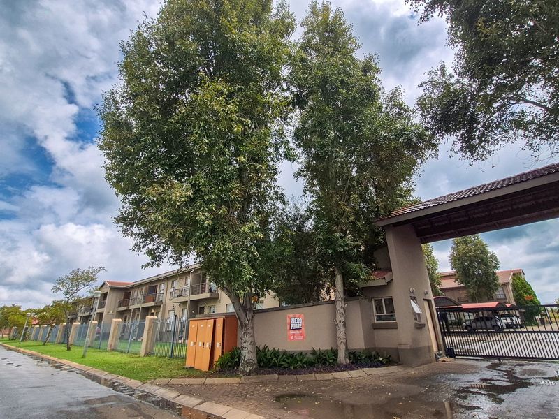 Front entrance view of the apartment complex featuring a secure gated access point, perimeter walling, and established trees.