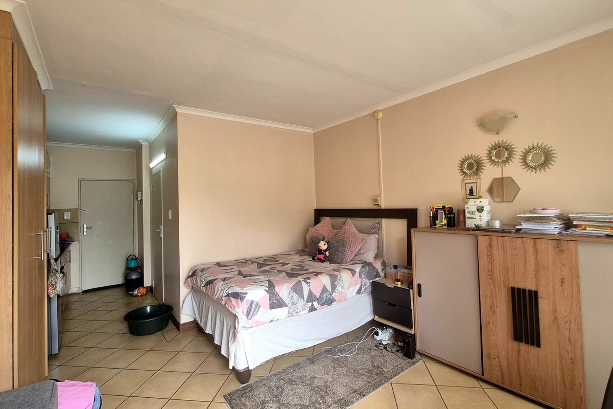A bedroom featuring tiled flooring, built-in wardrobe storage, and coved ceilings, with an open-plan layout leading towards the apartment entrance.
