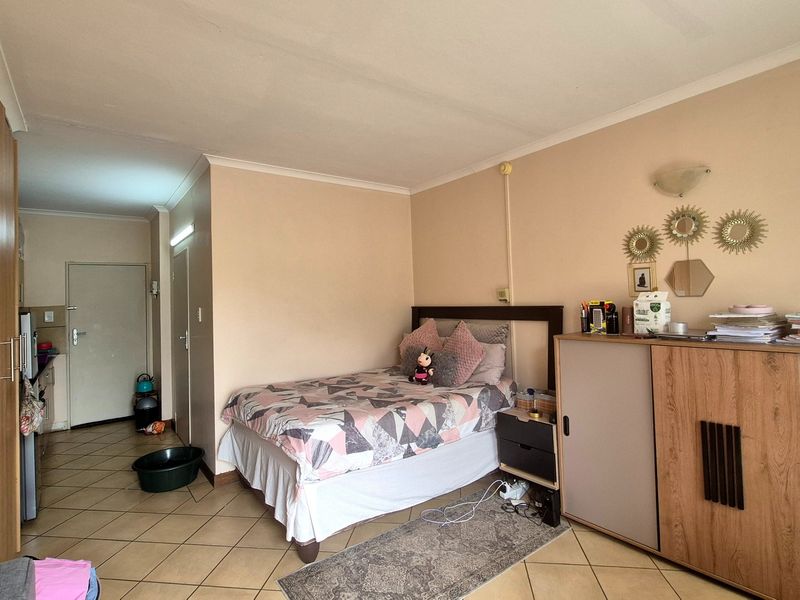 A bedroom featuring tiled flooring, built-in wardrobe storage, and coved ceilings, with an open-plan layout leading towards the apartment entrance.