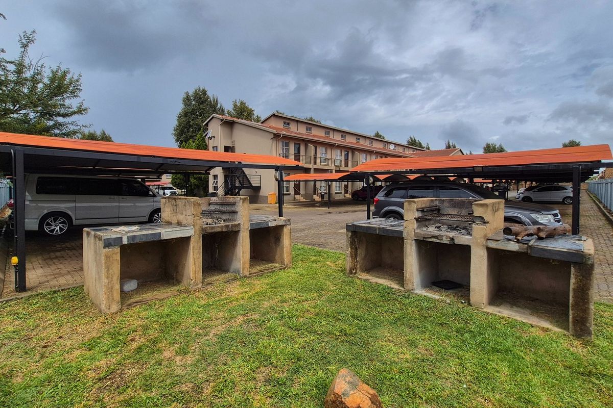 Communal outdoor area featuring built-in concrete braai facilities and covered parking bays within an apartment complex.