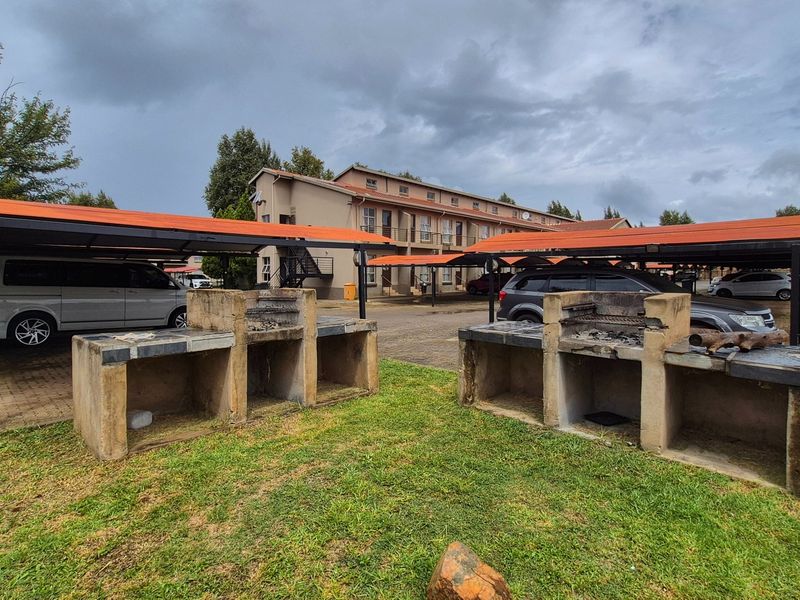 Communal outdoor area featuring built-in concrete braai facilities and covered parking bays within an apartment complex.