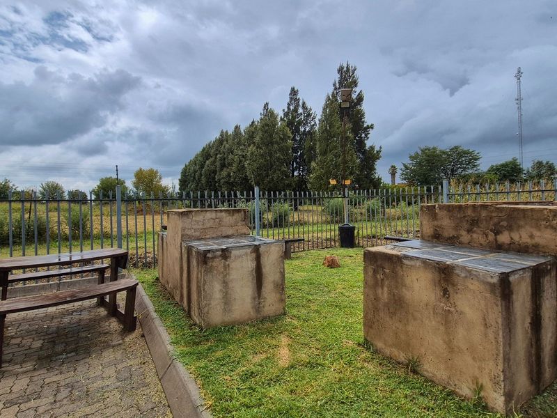 Outdoor communal area featuring built-in braai facilities and paved seating space, enclosed by metal perimeter fencing.