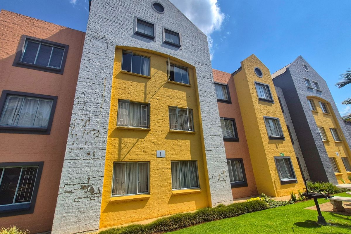 Exterior view of a multi-story apartment complex featuring colorful painted brick facades, casement windows with security bars, and a well-maintained lawn area.