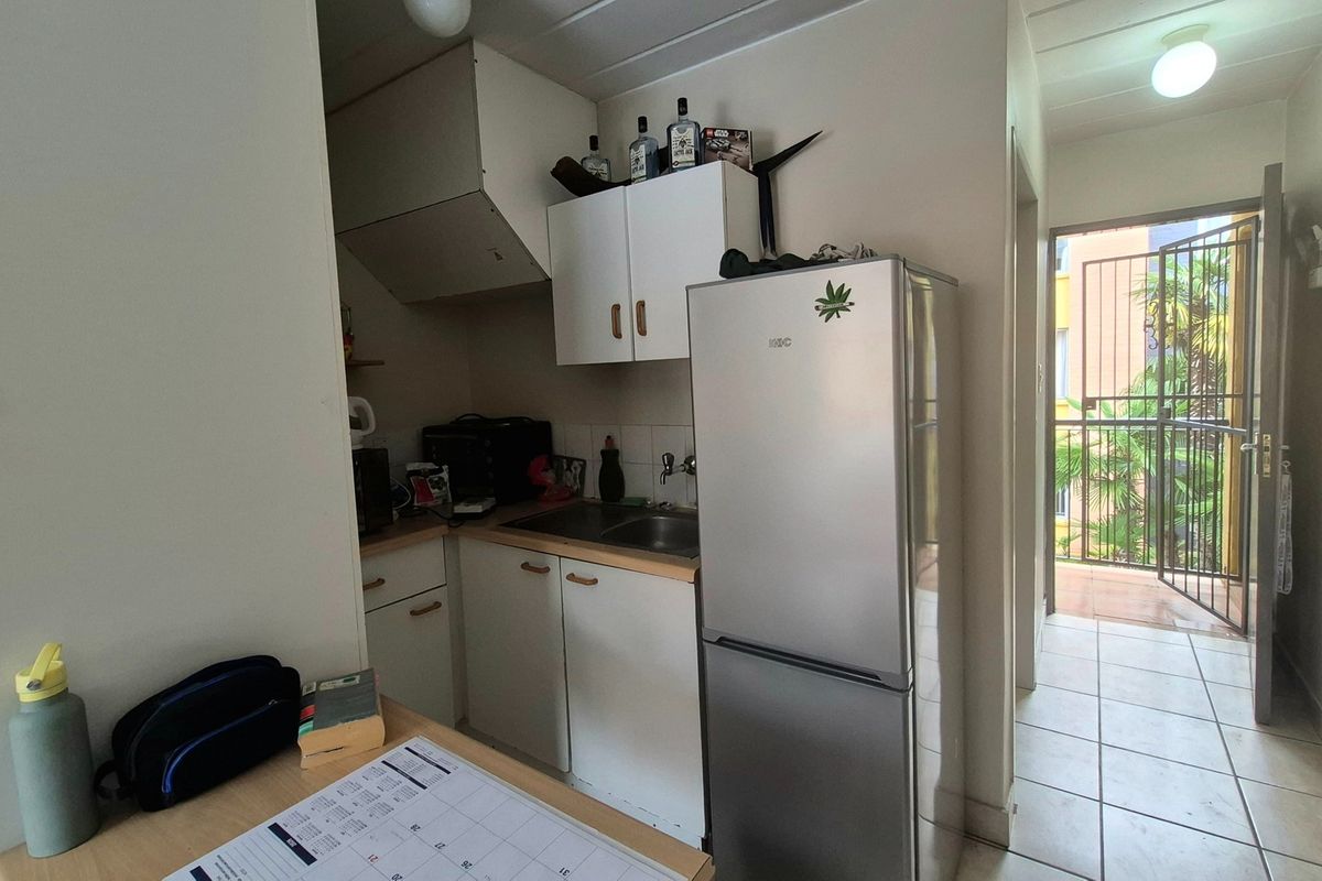 Compact kitchen area featuring built-in cabinetry, a stainless steel sink, and tiled flooring, with direct access to an outdoor balcony area.