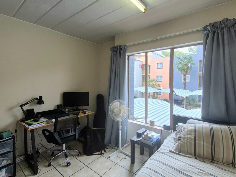 A functional bedroom featuring tiled flooring, a large window providing natural light, and standard ceiling lighting.
