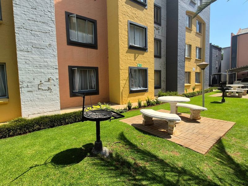 Communal garden area featuring a paved patio, fixed stone seating, and a built-in braai stand set against the apartment building exterior.