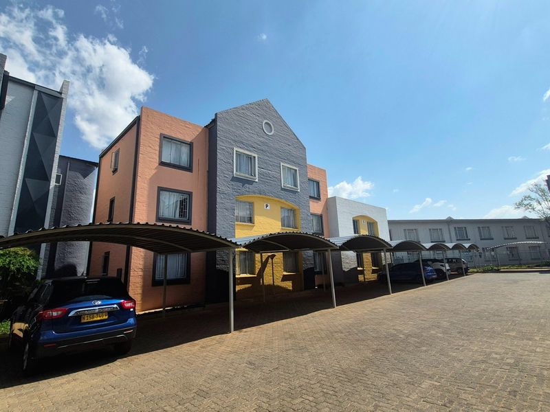Exterior view of a multi-story apartment complex featuring a paved driveway with covered parking bays and a multi-colored facade.