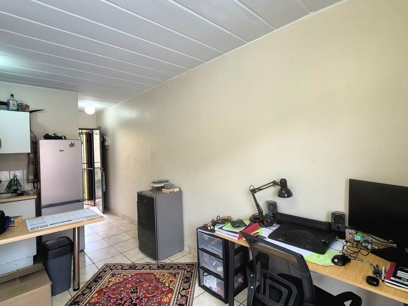 Open plan living area featuring tiled flooring, ceiling panels, and a compact kitchen corner with built-in cabinetry.