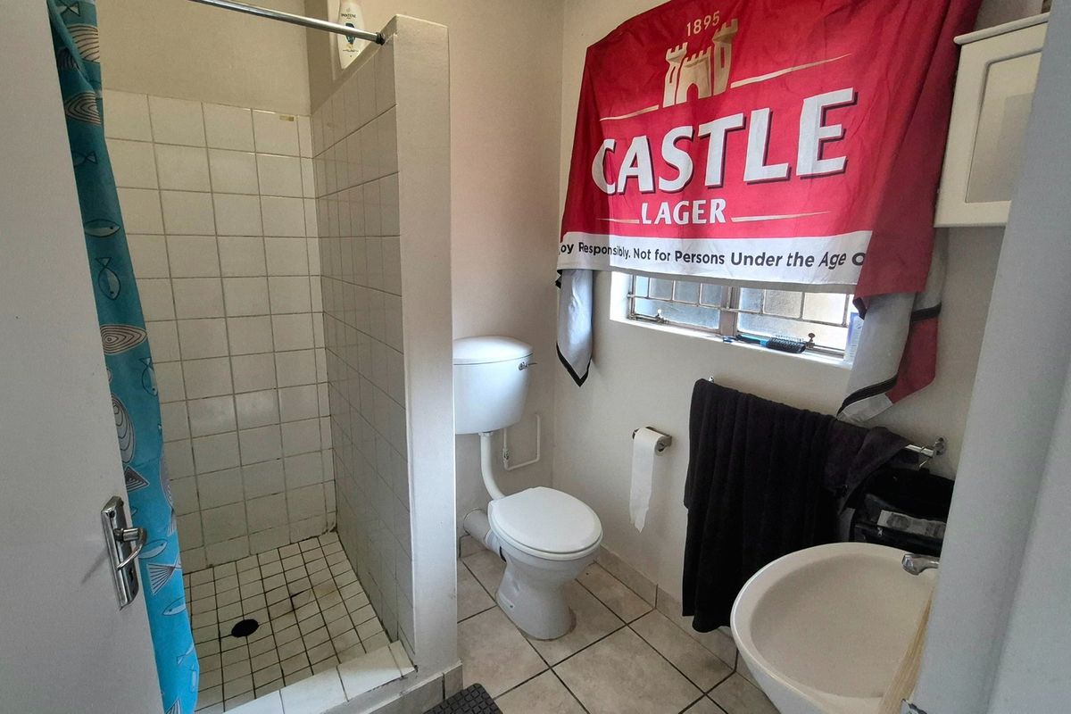 A functional bathroom featuring a shower cubicle, toilet, and washbasin with tiled flooring and walls, requiring cosmetic updates to improve its overall condition.