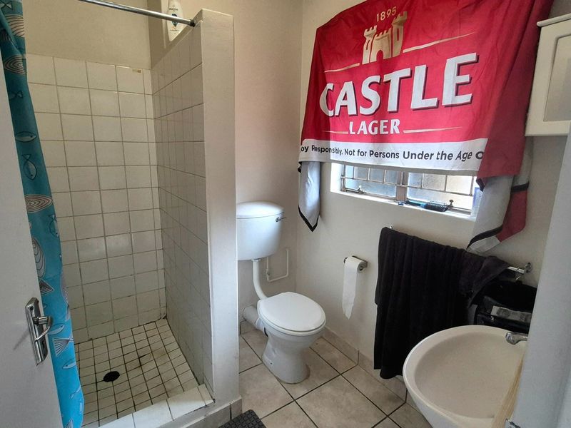 A functional bathroom featuring a shower cubicle, toilet, and washbasin with tiled flooring and walls, requiring cosmetic updates to improve its overall condition.