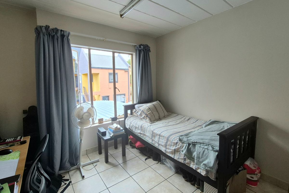A functional bedroom featuring tiled flooring and a large window that provides natural light, offering a neutral space ready for personalization.