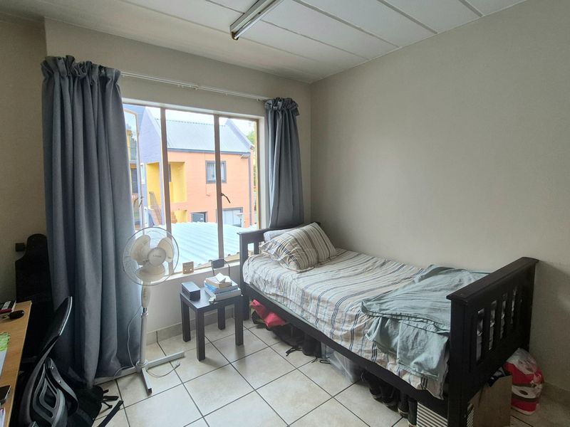 A functional bedroom featuring tiled flooring and a large window that provides natural light, offering a neutral space ready for personalization.