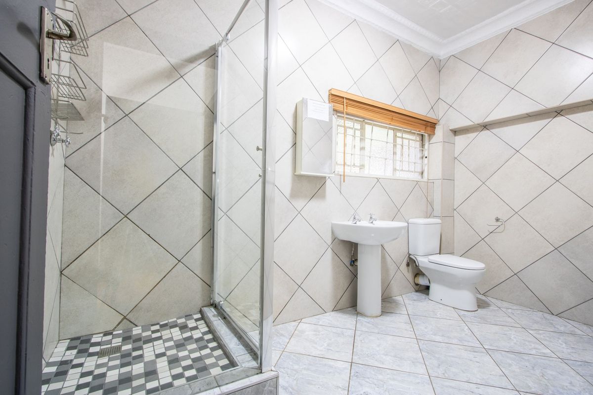 A clean, functional bathroom featuring a glass-enclosed shower, pedestal basin, toilet, and neutral tiled finishes throughout.