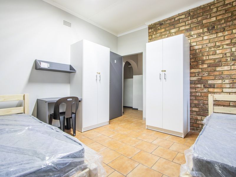 A functional bedroom featuring tiled flooring, an exposed brick feature wall, and built-in storage cupboards.