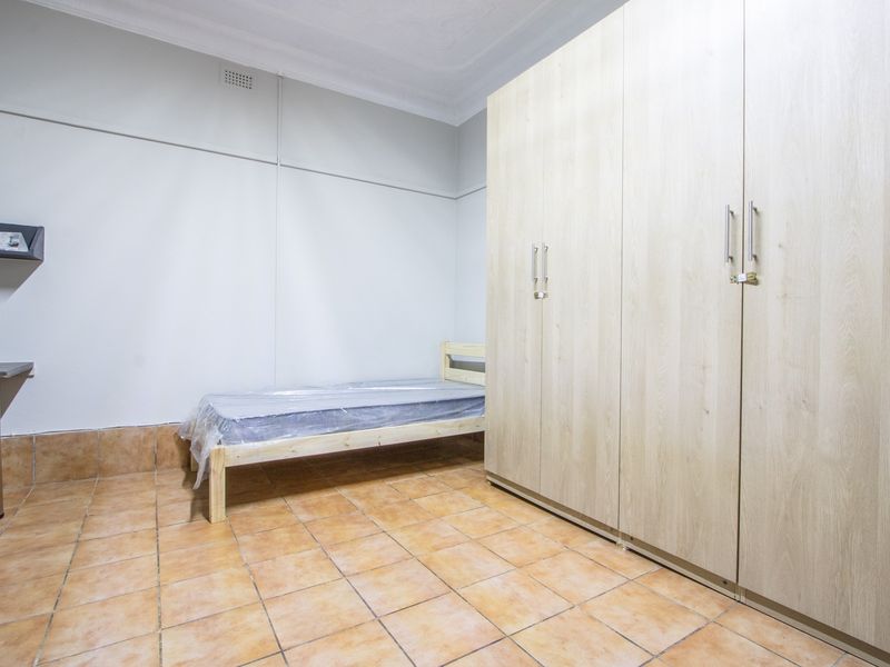 A functional bedroom featuring tiled flooring, a large built-in wardrobe, and neutral wall finishes.