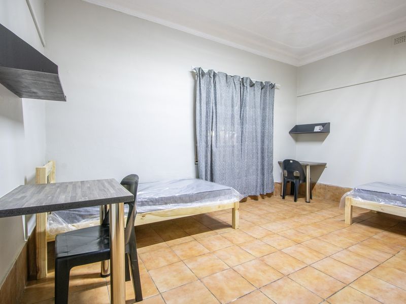 A functional bedroom featuring ceramic tile flooring, coved ceilings, and built-in shelving, providing a basic living space.
