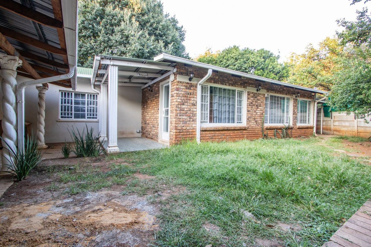 Rear view of a brick house featuring a covered patio area, white columns, and a garden space with lawn.