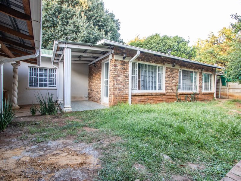 Rear view of a brick house featuring a covered patio area, white columns, and a garden space with lawn.