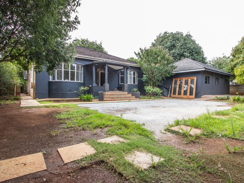 Front exterior view of a dark-painted house featuring a covered porch, bay windows, and a spacious driveway area.
