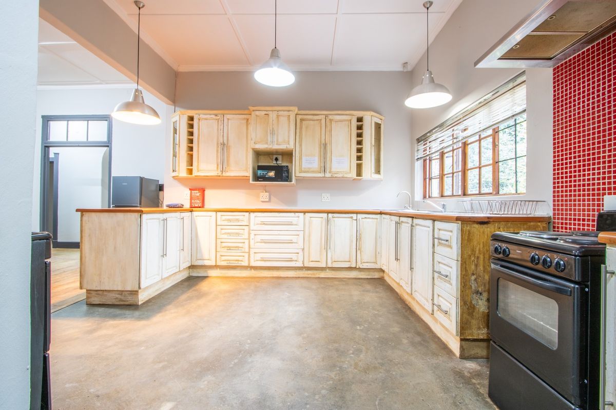 A spacious kitchen featuring rustic cabinetry, wooden countertops, a red tiled splashback, and concrete flooring, offering significant potential for a modern renovation.