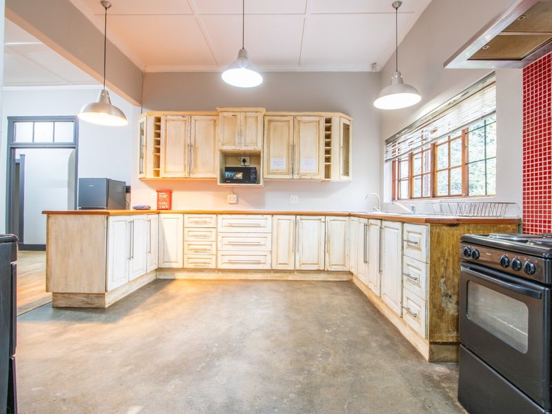 A spacious kitchen featuring rustic cabinetry, wooden countertops, a red tiled splashback, and concrete flooring, offering significant potential for a modern renovation.