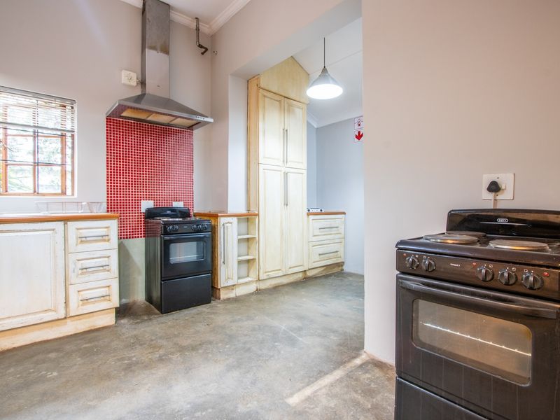 A functional kitchen area featuring built-in cabinetry, a red mosaic tile splashback, stainless steel extractor fan, and concrete flooring.