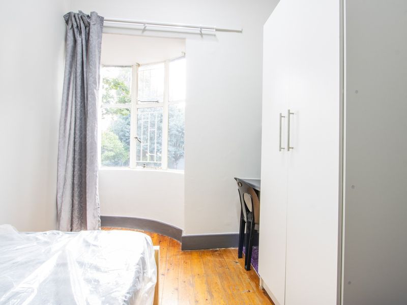 A bedroom featuring polished timber flooring, a bay window, and a built-in wardrobe.