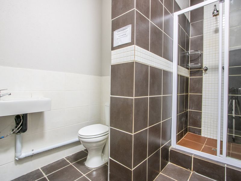 A functional bathroom featuring a wall-mounted basin, toilet, and a tiled shower enclosure with a glass door.