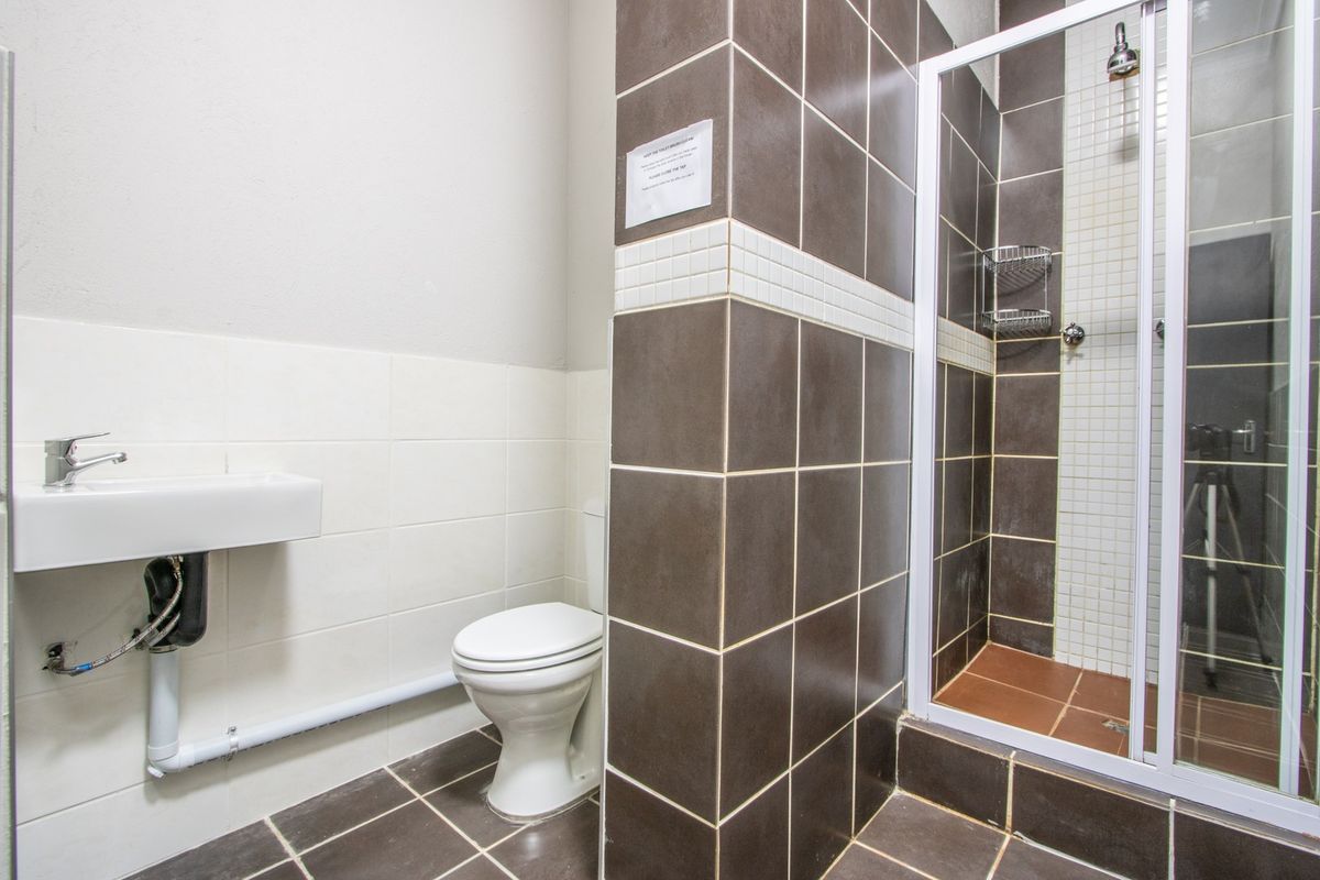 A functional bathroom featuring a wall-mounted basin, toilet, and a tiled shower enclosure with a glass door.