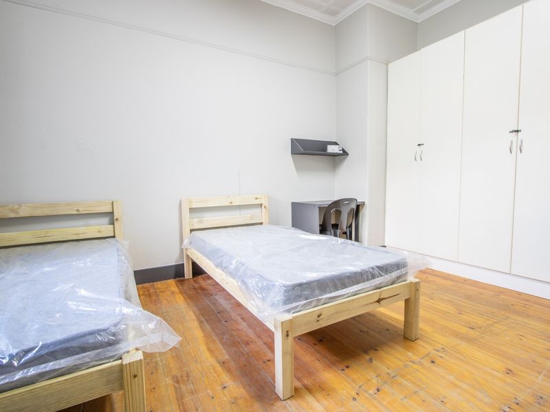 A bedroom featuring polished wooden flooring, built-in white cupboards, and classic architectural details like picture rails and cornices.