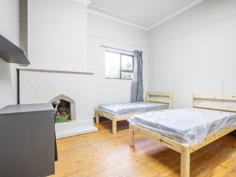 A bedroom featuring original timber flooring, a decorative fireplace, and high ceilings with traditional cornicing.