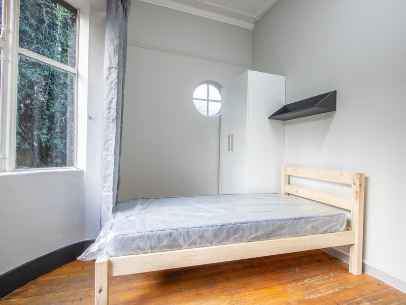 A bedroom featuring original timber flooring, a unique circular window, and a built-in wardrobe, offering a bright and functional living space.