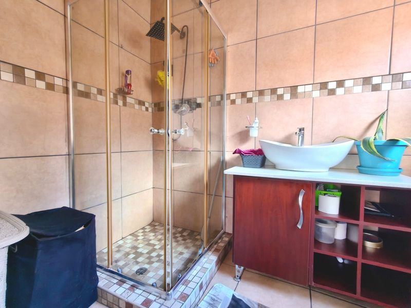 A functional bathroom featuring a glass-enclosed shower, a modern vessel sink set on a wooden vanity cabinet, and neutral-toned wall tiling.