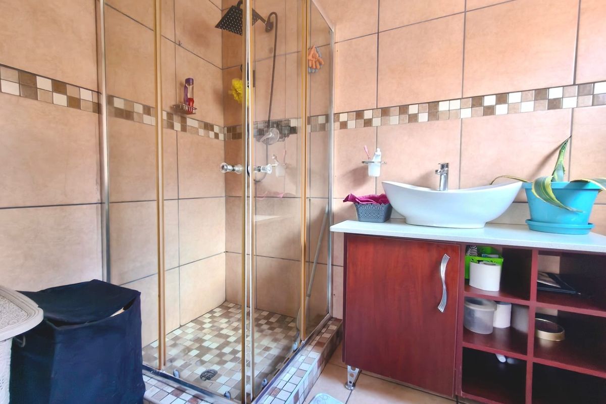 A functional bathroom featuring a glass-enclosed shower, a modern vessel sink set on a wooden vanity cabinet, and neutral-toned wall tiling.
