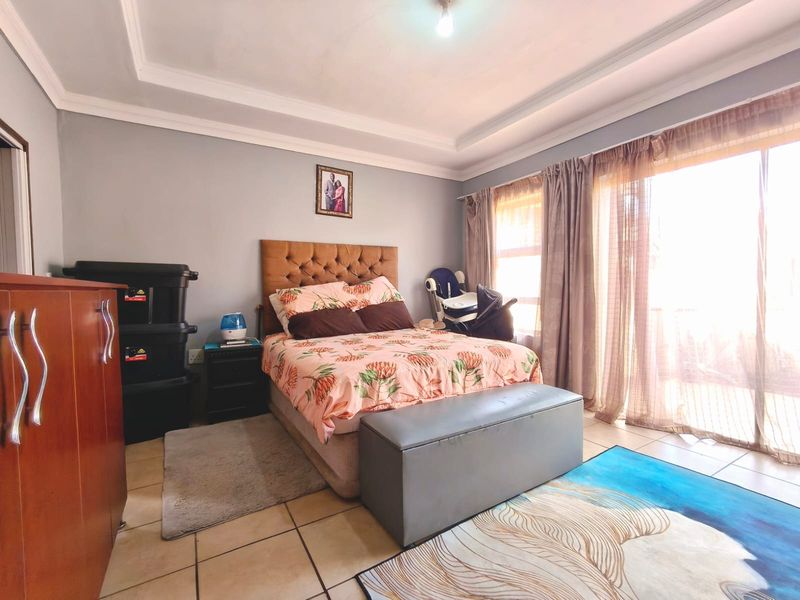 A bedroom featuring tiled flooring, a tray ceiling, and large sliding glass doors that provide access to the exterior.