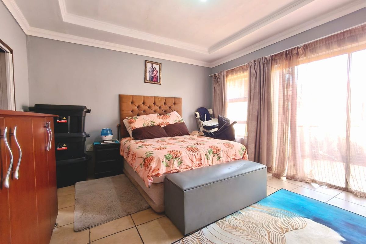 A bedroom featuring tiled flooring, a tray ceiling, and large sliding glass doors that provide access to the exterior.