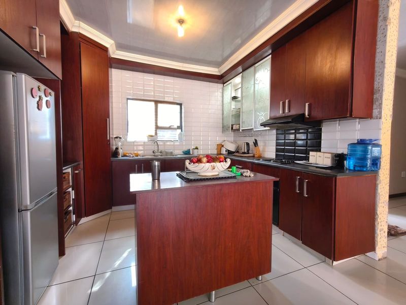 A functional kitchen featuring dark wood cabinetry, a central island, tiled backsplash, and tiled flooring, providing ample storage and workspace.