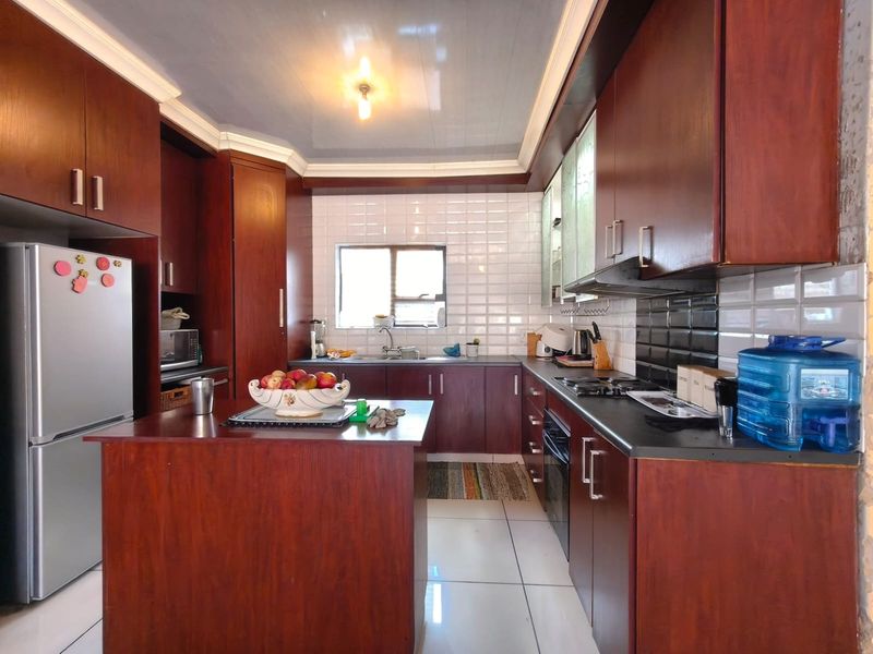 A functional kitchen featuring dark wood cabinetry, a central island, built-in oven and hob, and white tiled flooring.
