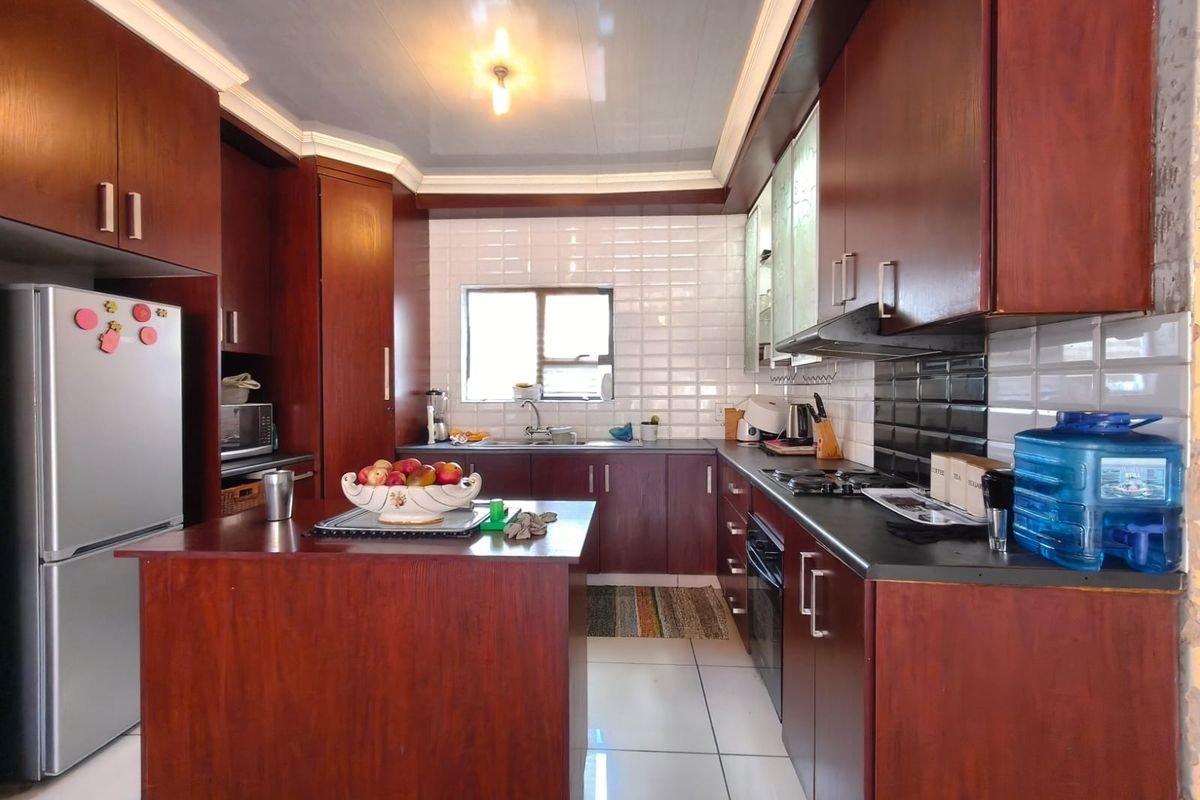 A functional kitchen featuring dark wood cabinetry, a central island, built-in oven and hob, and white tiled flooring.