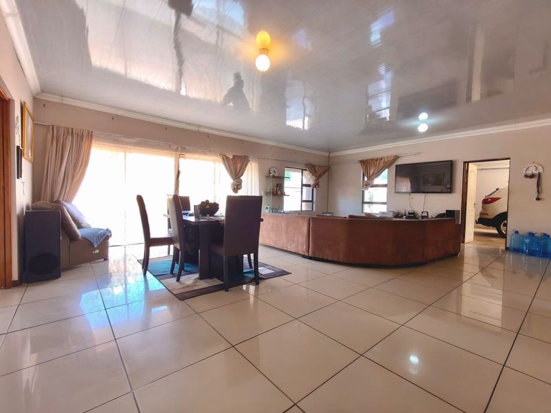 Spacious open-plan living and dining area featuring glossy ceilings, large ceramic floor tiles, and sliding glass doors leading to the exterior.