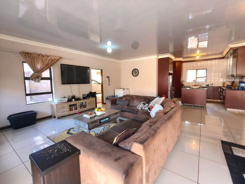 Spacious open-plan living area featuring tiled flooring, a glossy ceiling, and a functional kitchen with built-in cabinetry and a central island.