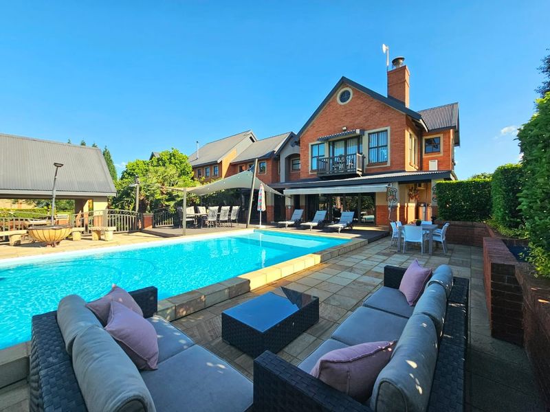 Spacious outdoor pool area featuring a large swimming pool, paved patio, retractable awning, and a multi-story brick residence with a balcony.