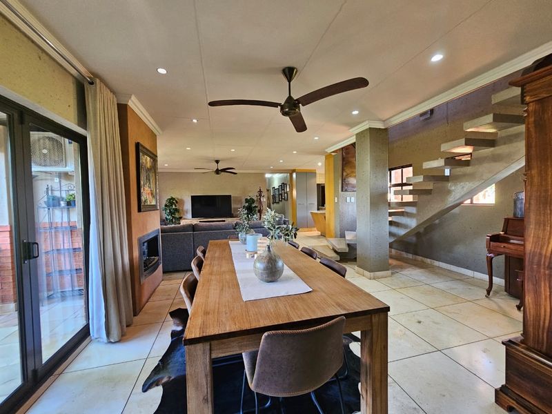 Spacious open-plan living and dining area featuring a modern floating staircase, fireplace, tiled flooring, and large sliding doors leading to the patio.