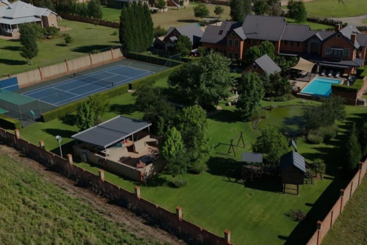 Aerial view of a large residential property featuring a tennis court, swimming pool, landscaped garden, pond, and a covered outdoor entertainment area.