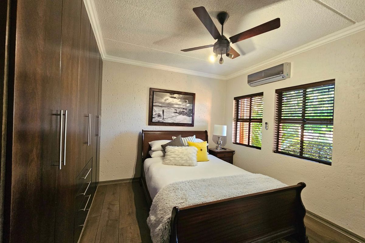 A well-maintained bedroom featuring dark wood built-in cupboards, laminate flooring, a ceiling fan, and a wall-mounted air conditioning unit.